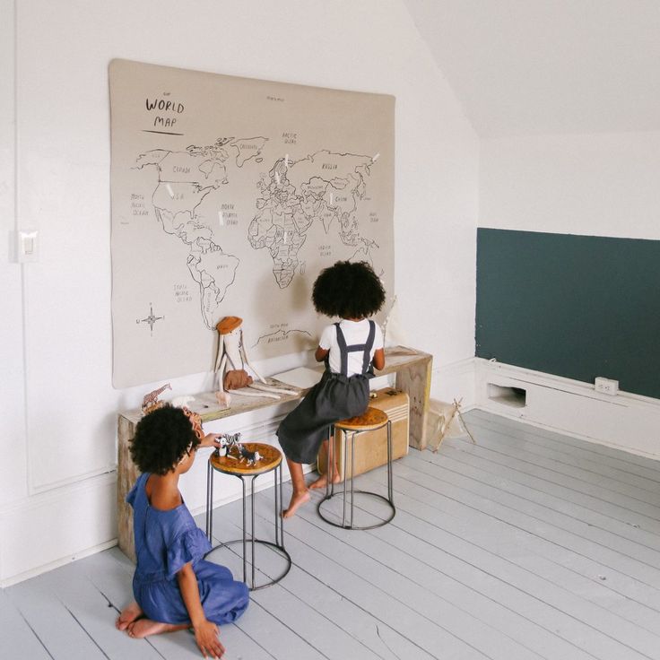 two children sitting on stools in front of a chalkboard with a world map drawn on it