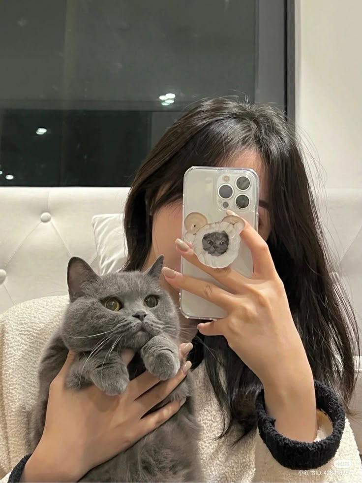 a woman holding a cat and taking a selfie with her cell phone in front of her face