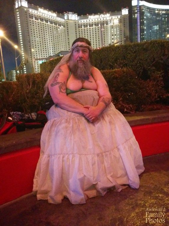 a man in a wedding dress sitting on a red bench with his arms folded out