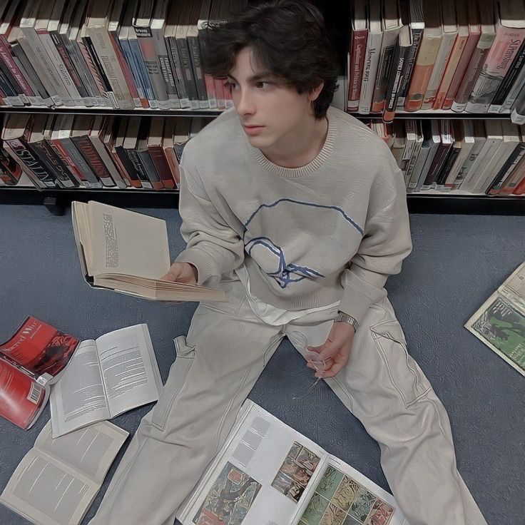 a young man sitting on the floor in front of a book shelf filled with books