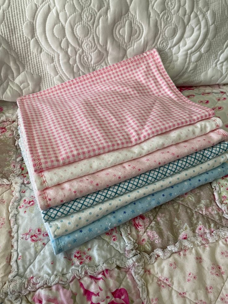 a pile of quilts sitting on top of a bed covered in pink and white flowers