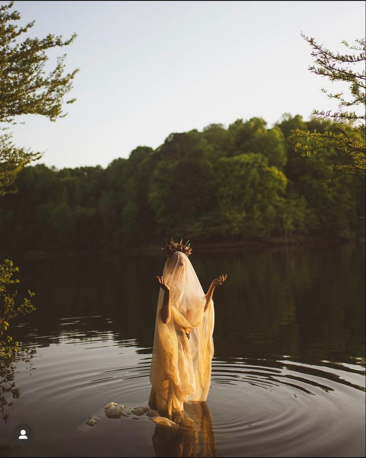 a woman is standing in the water wearing a yellow dress and holding her hands up