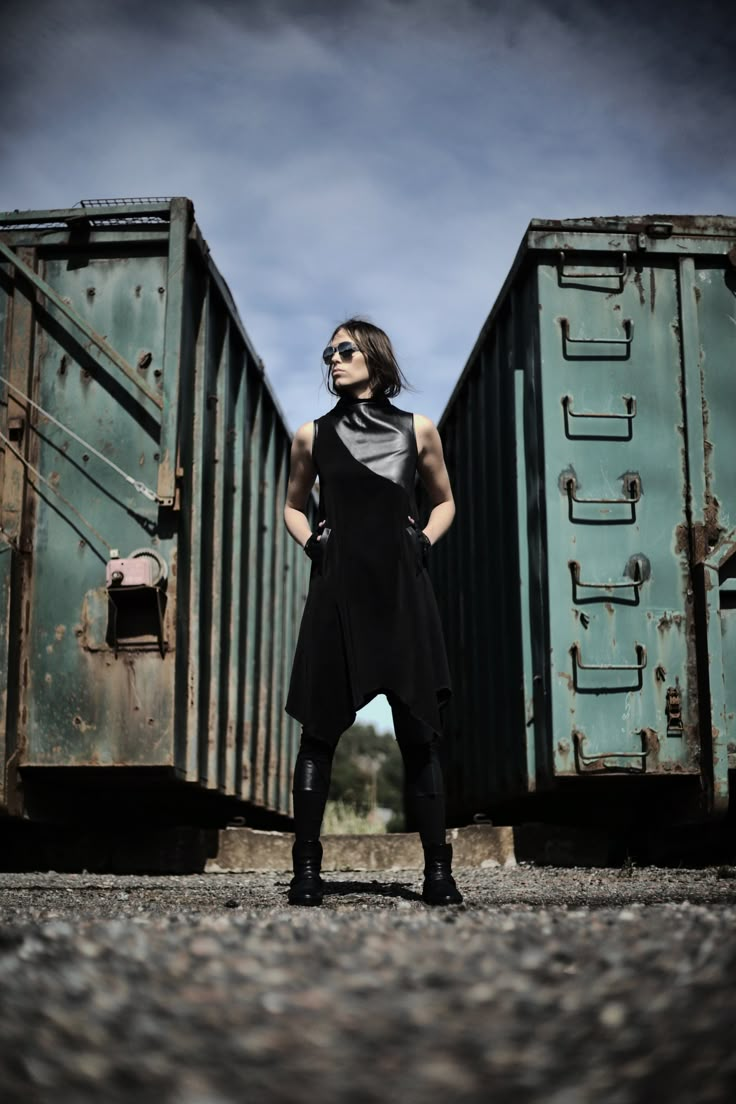 a woman standing in front of two train cars with her hands on her hips and looking at the camera