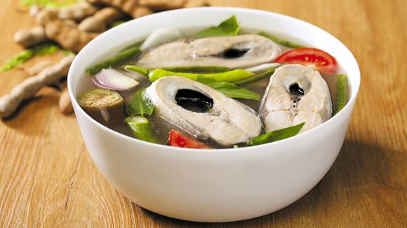 a white bowl filled with fish and vegetables on top of a wooden table next to sliced ginger