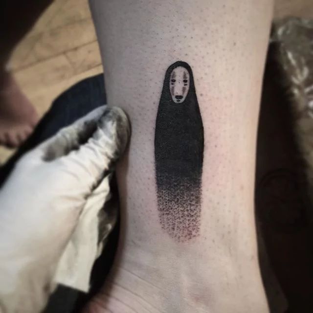 a woman's foot with a black and white spirited ghost tattoo on her left ankle