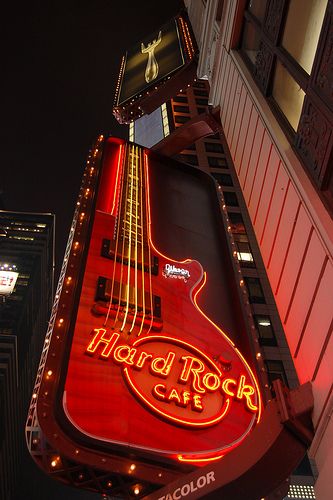 the neon sign for hard rock cafe is lit up in front of tall buildings at night