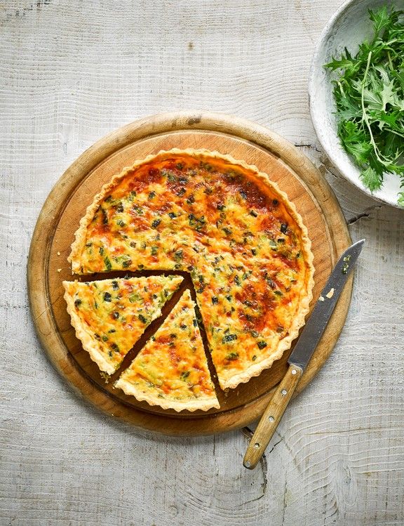 a quiche on a wooden platter with one slice cut out