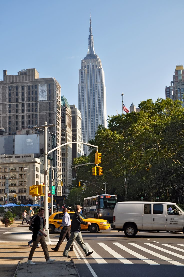 several people crossing the street in front of tall buildings and skyscrapers on a sunny day