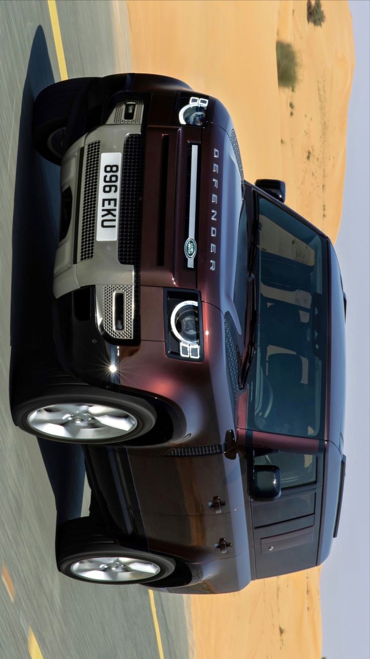 the front end of a black truck with its lights on driving down a road next to a sandy beach