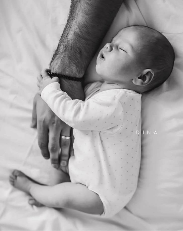 a black and white photo of a baby holding the arm of an adult