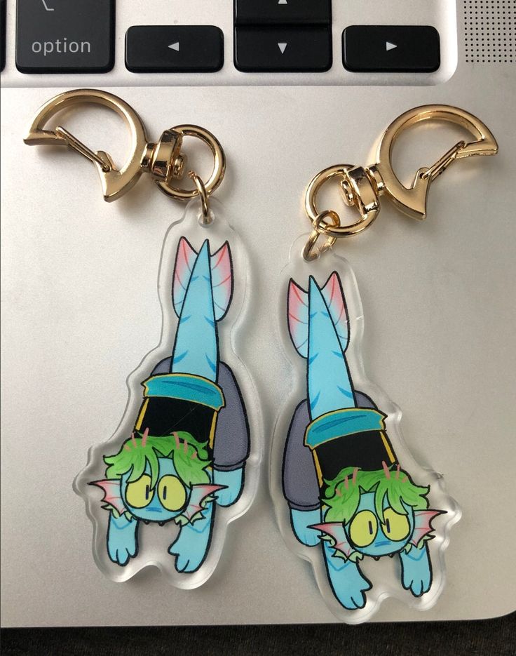 two keychains with cartoon characters on them sitting next to a laptop computer keyboard