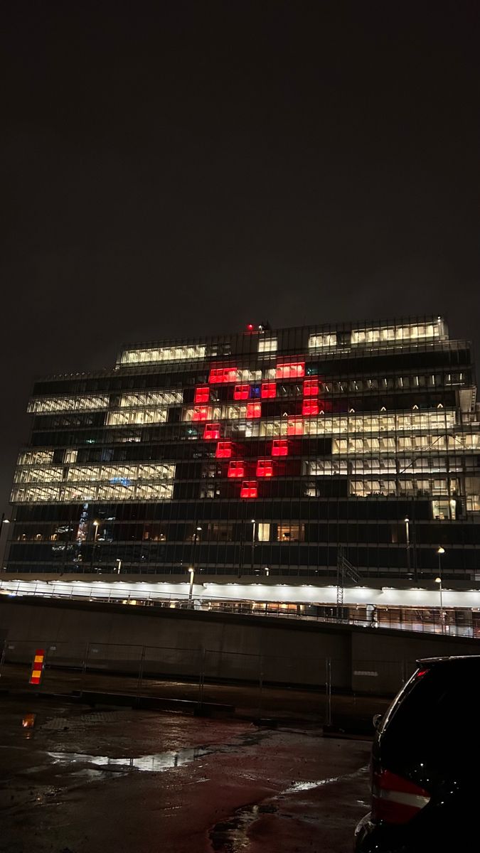 a large building lit up at night with red lights on it's side and cars parked in front