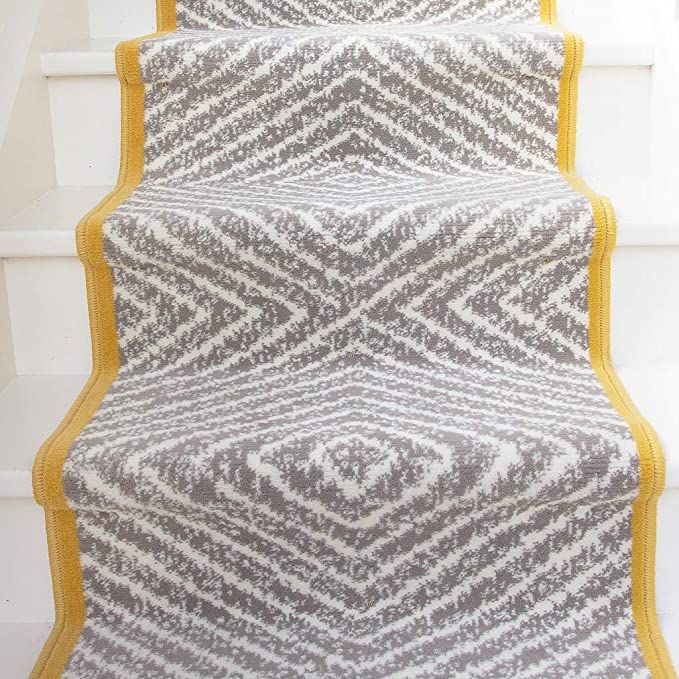 a carpeted stair case with yellow trim on the bottom, and an area rug underneath it