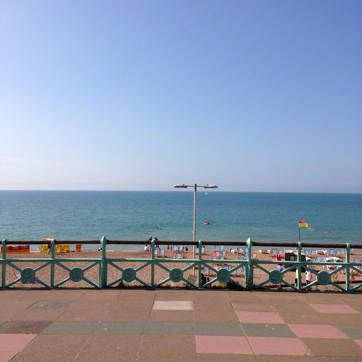 people are sitting on benches near the beach and looking out at the ocean from a pier