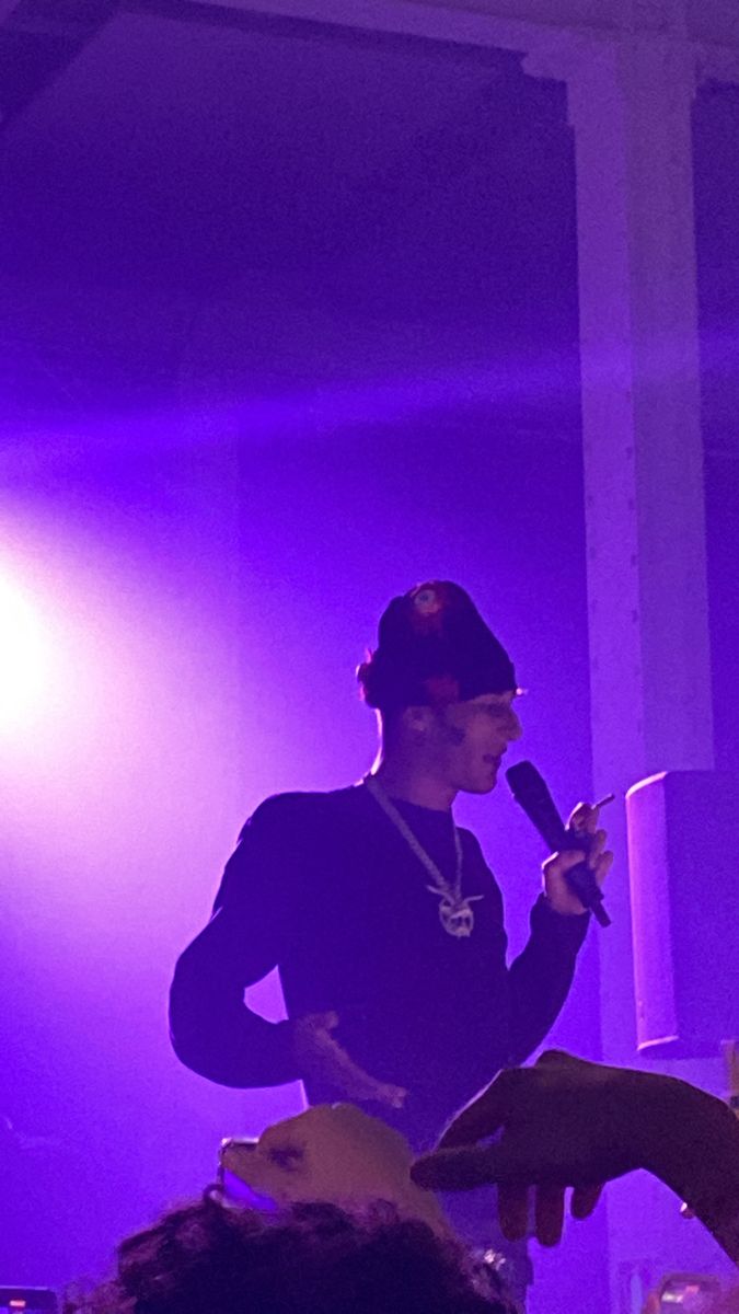 a man standing in front of a microphone on top of a purple light filled stage