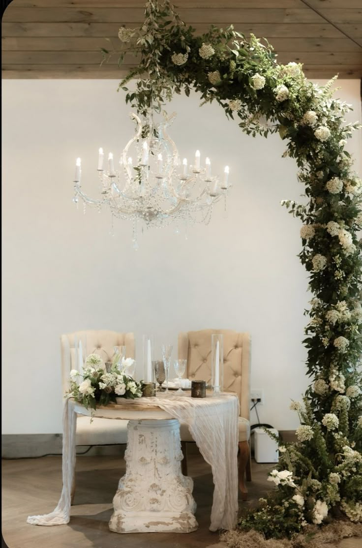 the table is set with white flowers and greenery on it, along with candles