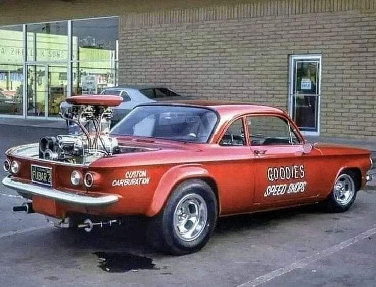 an old red car parked in front of a building with a motorcycle engine on it's hood