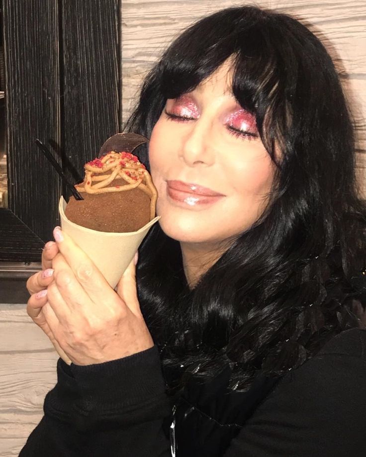 a woman is holding an ice cream cone with chocolate frosting on it and looking at the camera