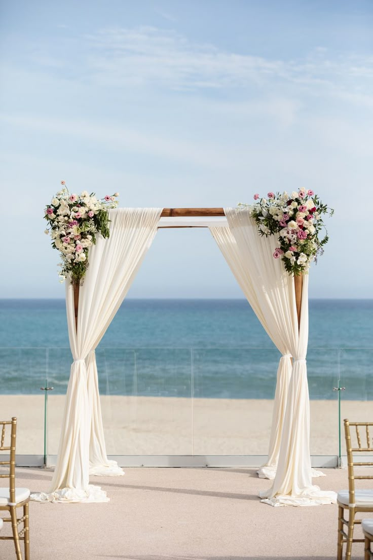 an outdoor wedding ceremony setup with white drapes and flowers on the altar, overlooking the ocean