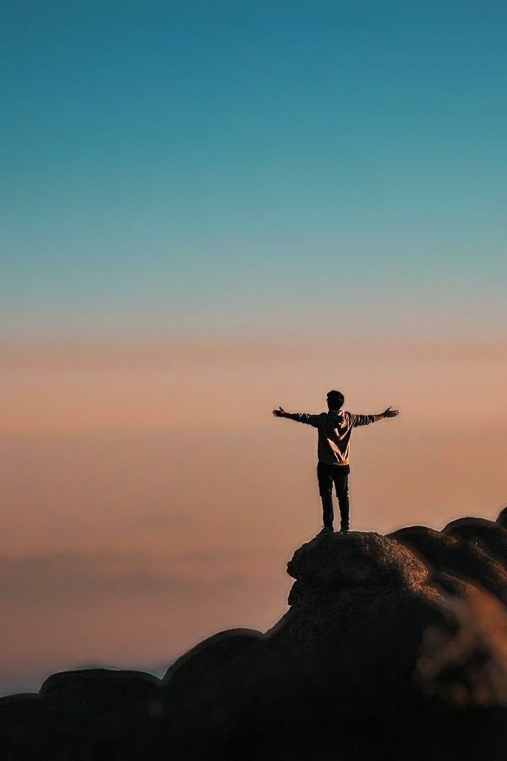 a man standing on top of a large rock with his arms spread out in the air