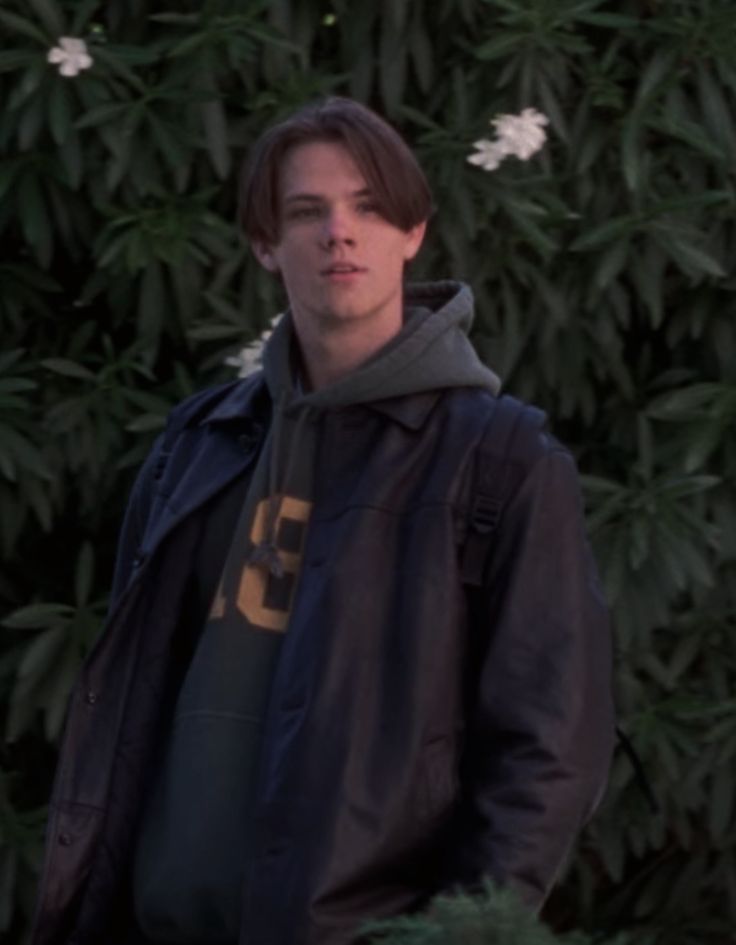 a young man standing in front of some bushes