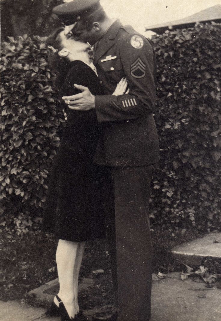 an old black and white photo of a man in uniform kissing a woman on the cheek