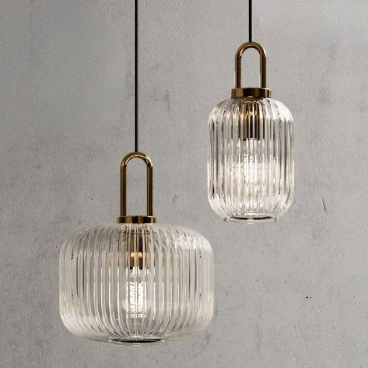 two clear glass pendant lights hanging from a ceiling fixture in a room with concrete walls