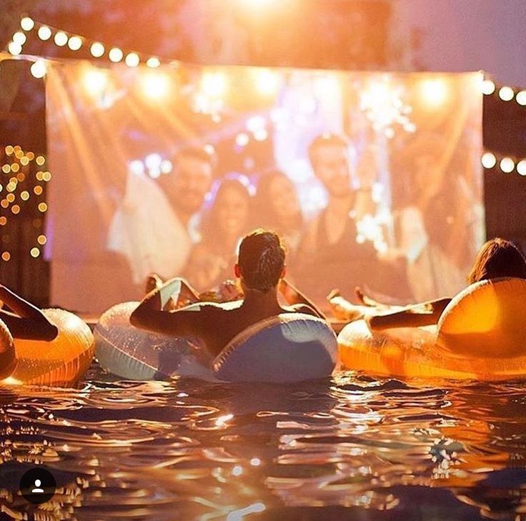 people are in the water watching a movie on an outdoor projector screen at night