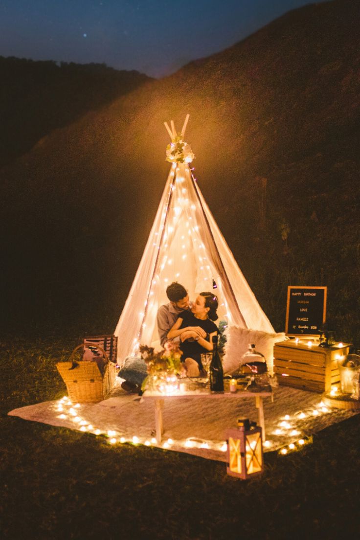 a man and woman are sitting in front of a teepee with lights on it