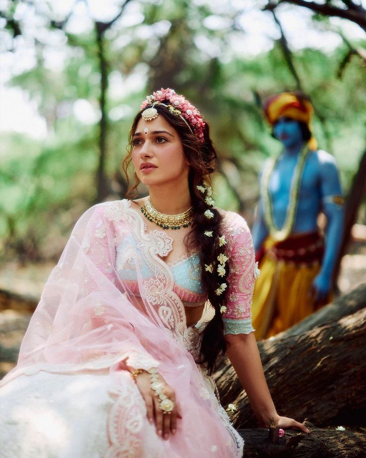 a woman sitting on top of a tree branch wearing a pink and white sari