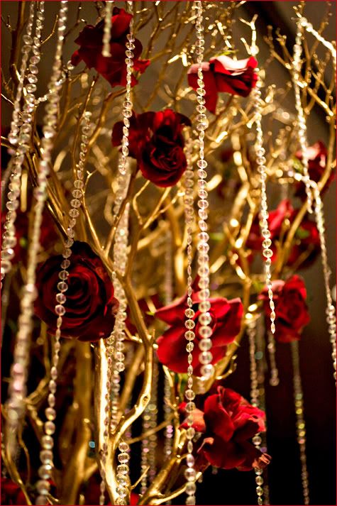 some red roses and beads hanging from a gold colored tree with long, thin branches