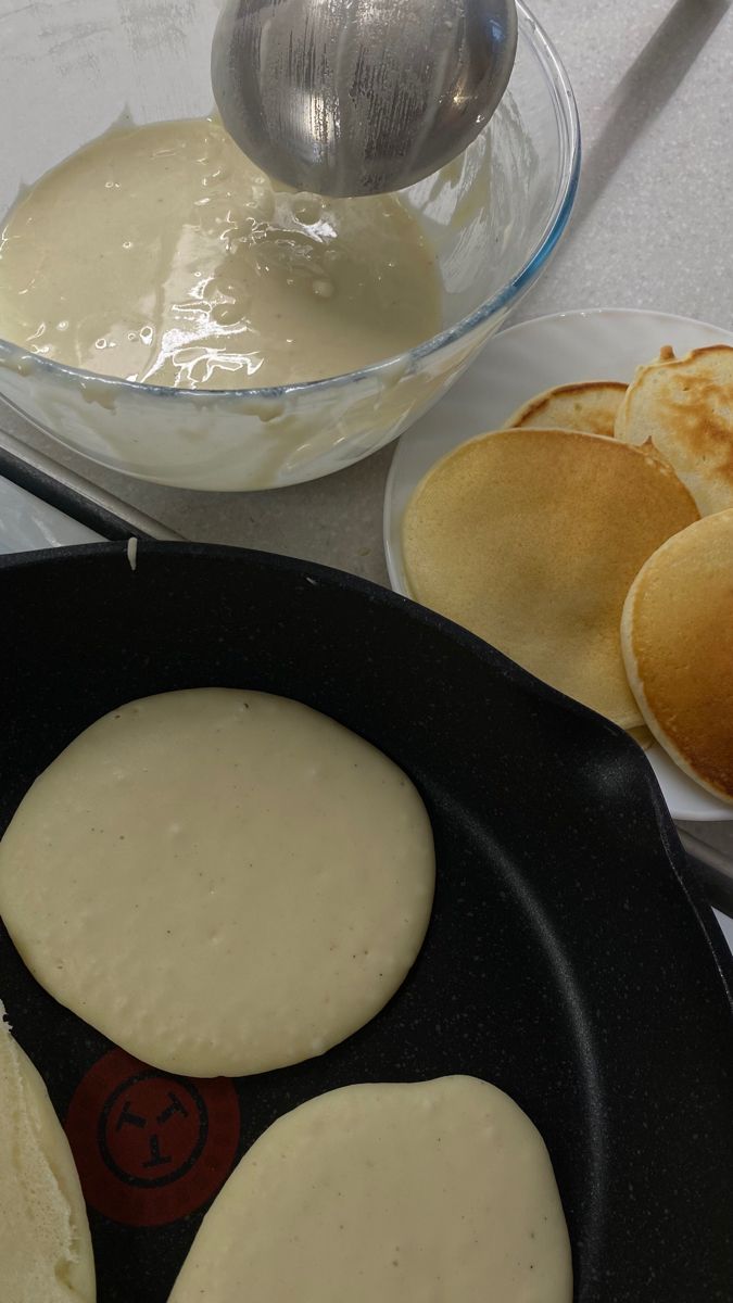 pancakes being cooked in a skillet with butter and syrup on the table next to it