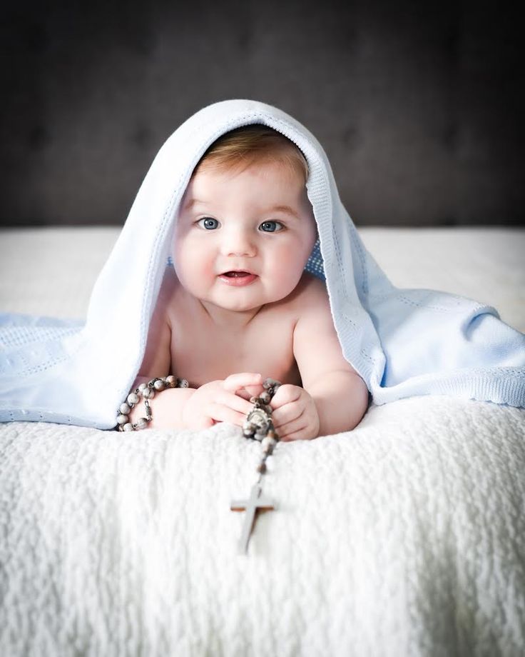 a baby laying on top of a bed under a blanket with a cross hanging from it's side