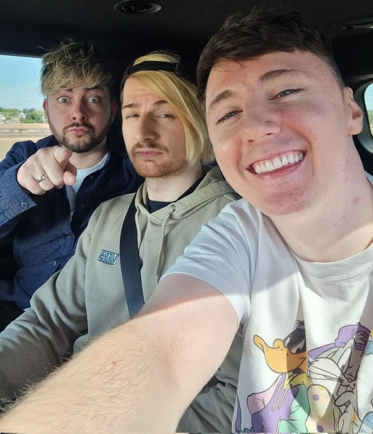 three men sitting in the back seat of a car with one pointing at the camera