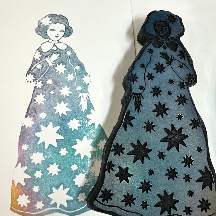 two handmade paper dolls are next to each other on a white tablecloth with black and blue stars