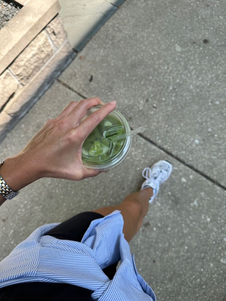 a person holding a cup of green tea on the sidewalk