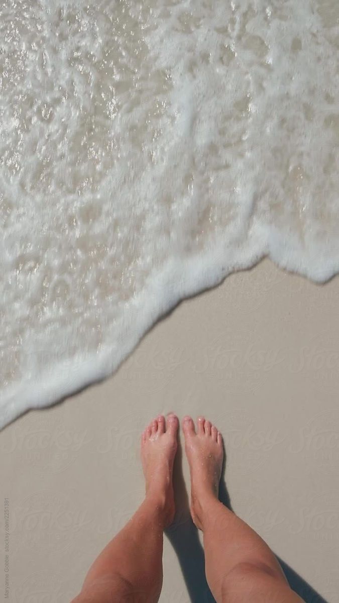 two people standing on the beach with their feet in the water