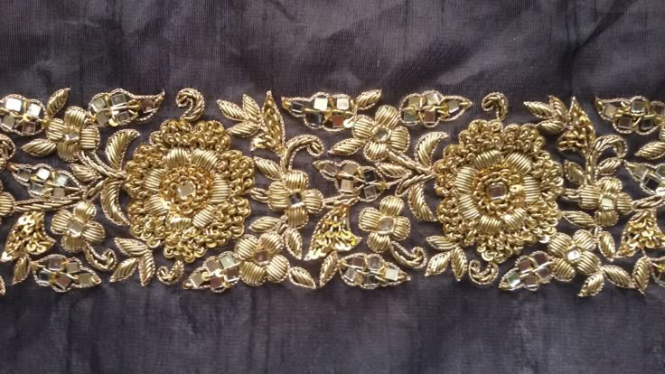 a gold embroidered belt with flowers and leaves on black velvet background, close up view