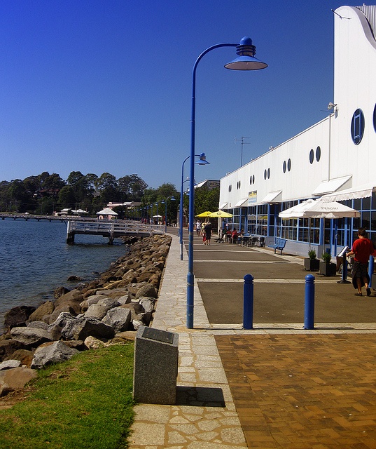 people are walking on the sidewalk by the water