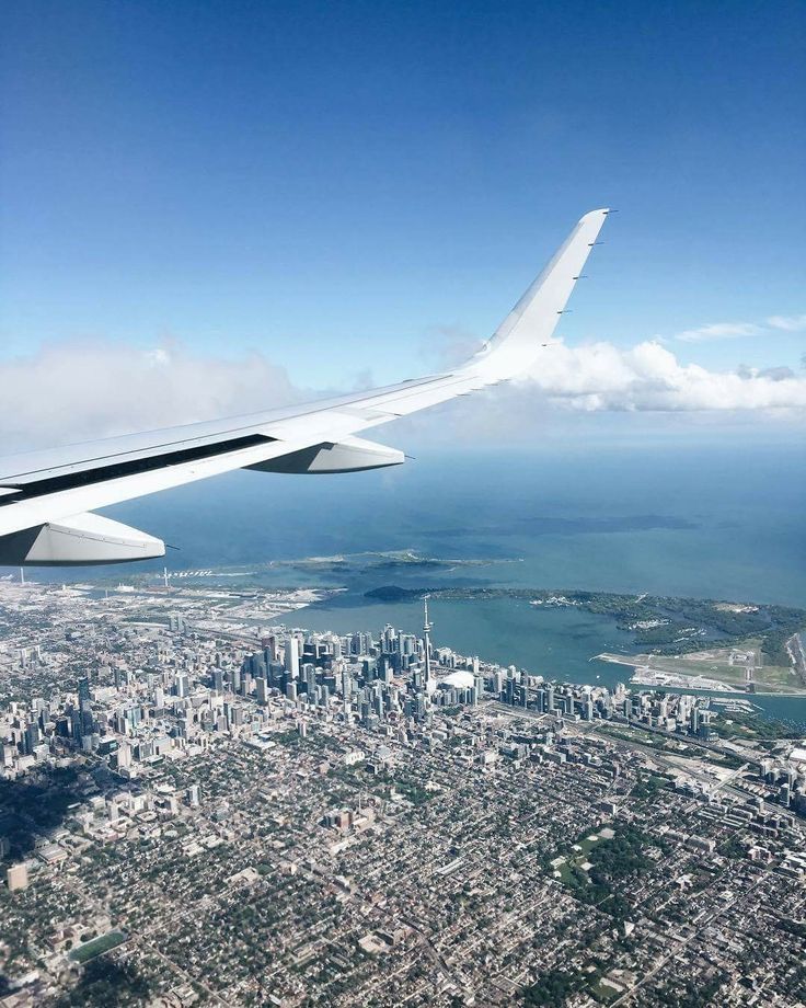 the wing of an airplane flying over a large city and ocean with clouds in the sky