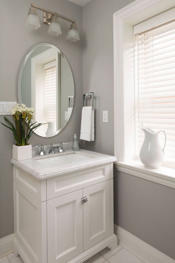 a white sink sitting under a bathroom mirror next to a vase with flowers in it