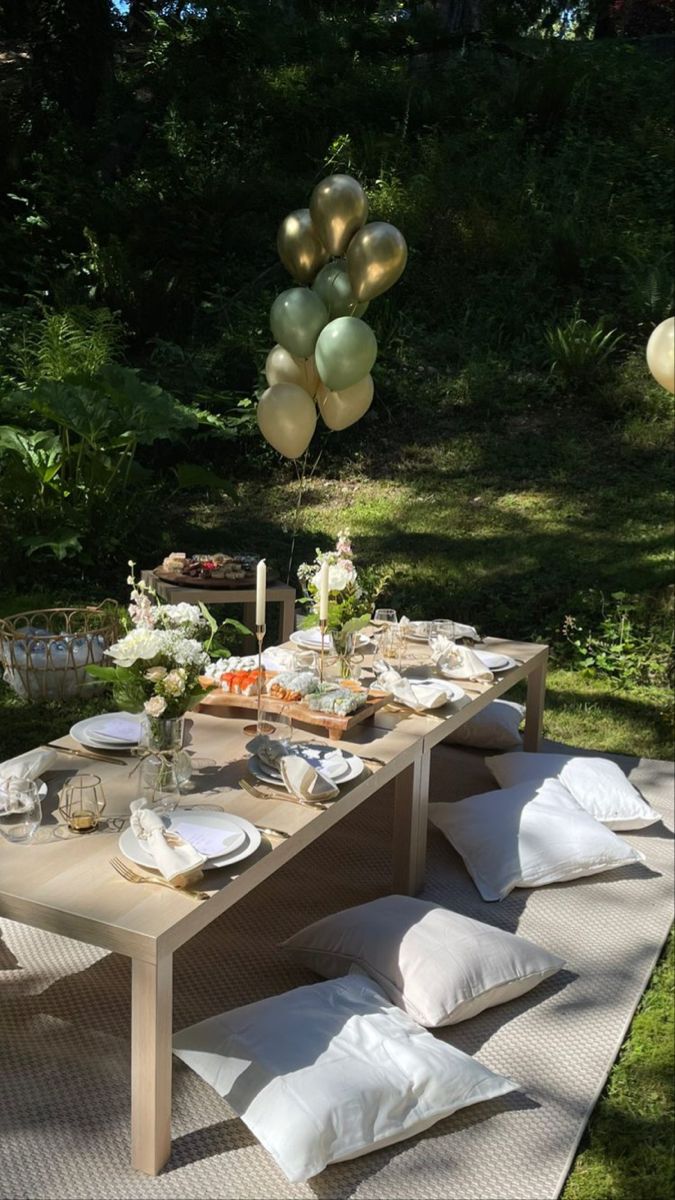 an outdoor table set up for a party with balloons in the air and food on it