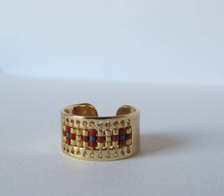 a gold ring with red and yellow squares on it's sides, sitting on a white surface