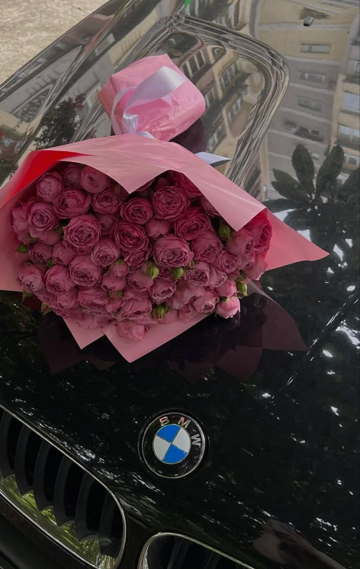 a bunch of pink roses sitting on the hood of a black bmw parked in front of a building