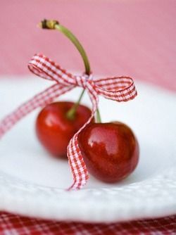 two cherries on a white plate with a red and white checkered table cloth