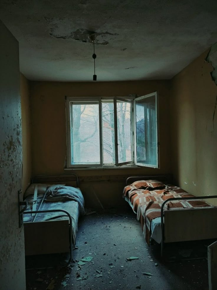 an empty room with two beds and a window in the corner that is partially open