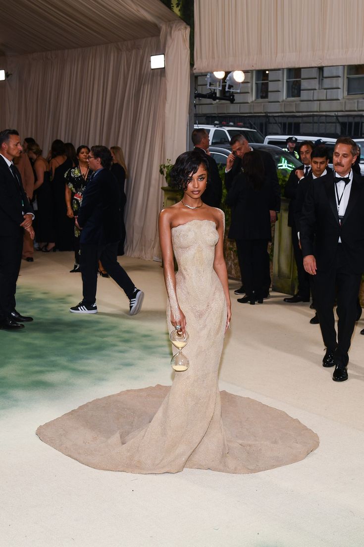 a woman in a strapless dress standing on a carpet with other people around her