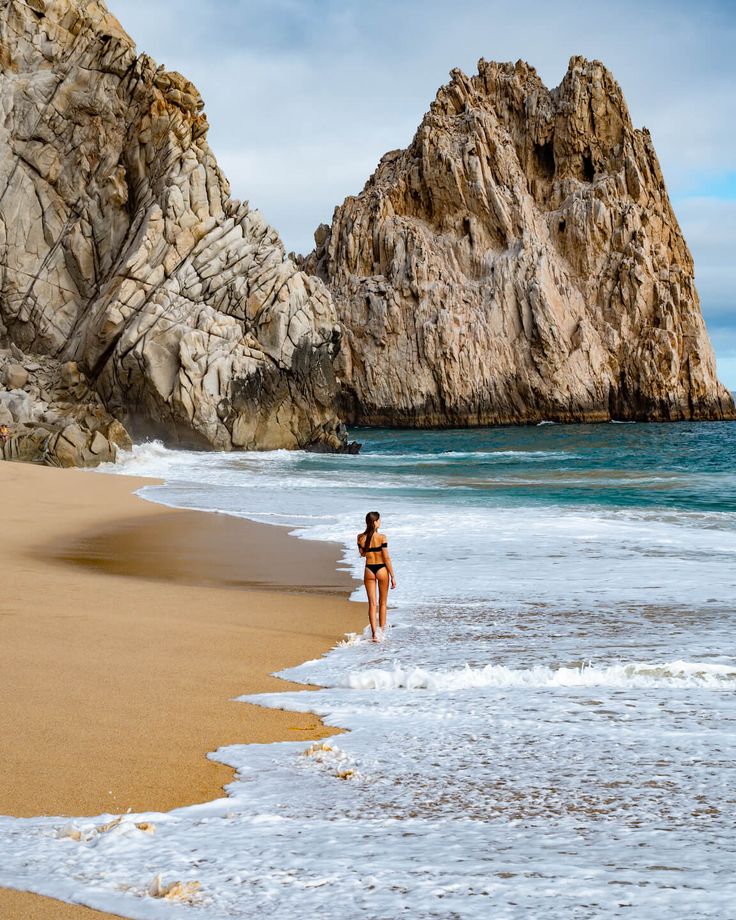 a woman walking on the beach next to some rocks