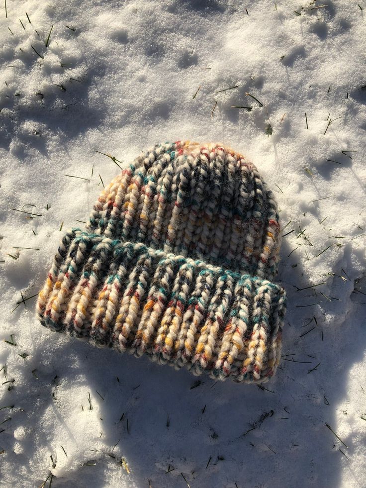 a knitted hat laying in the snow on top of some grass and snow covered ground