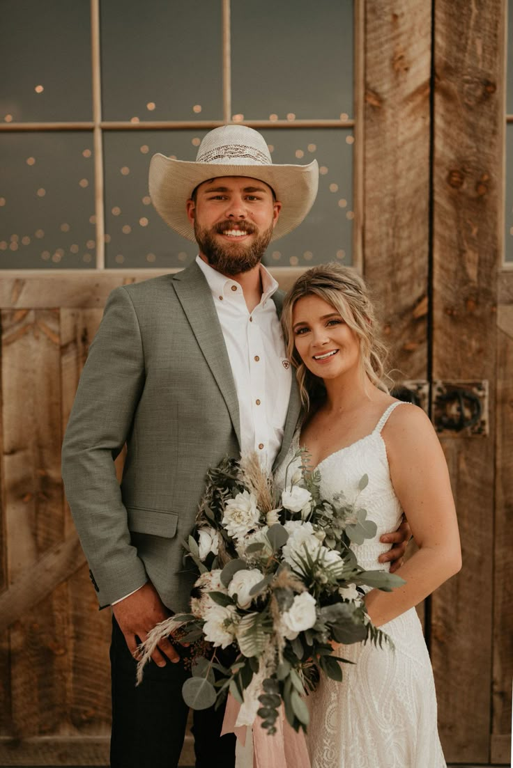 a bride and groom pose for a photo in front of an old barn door wearing cowboy hats